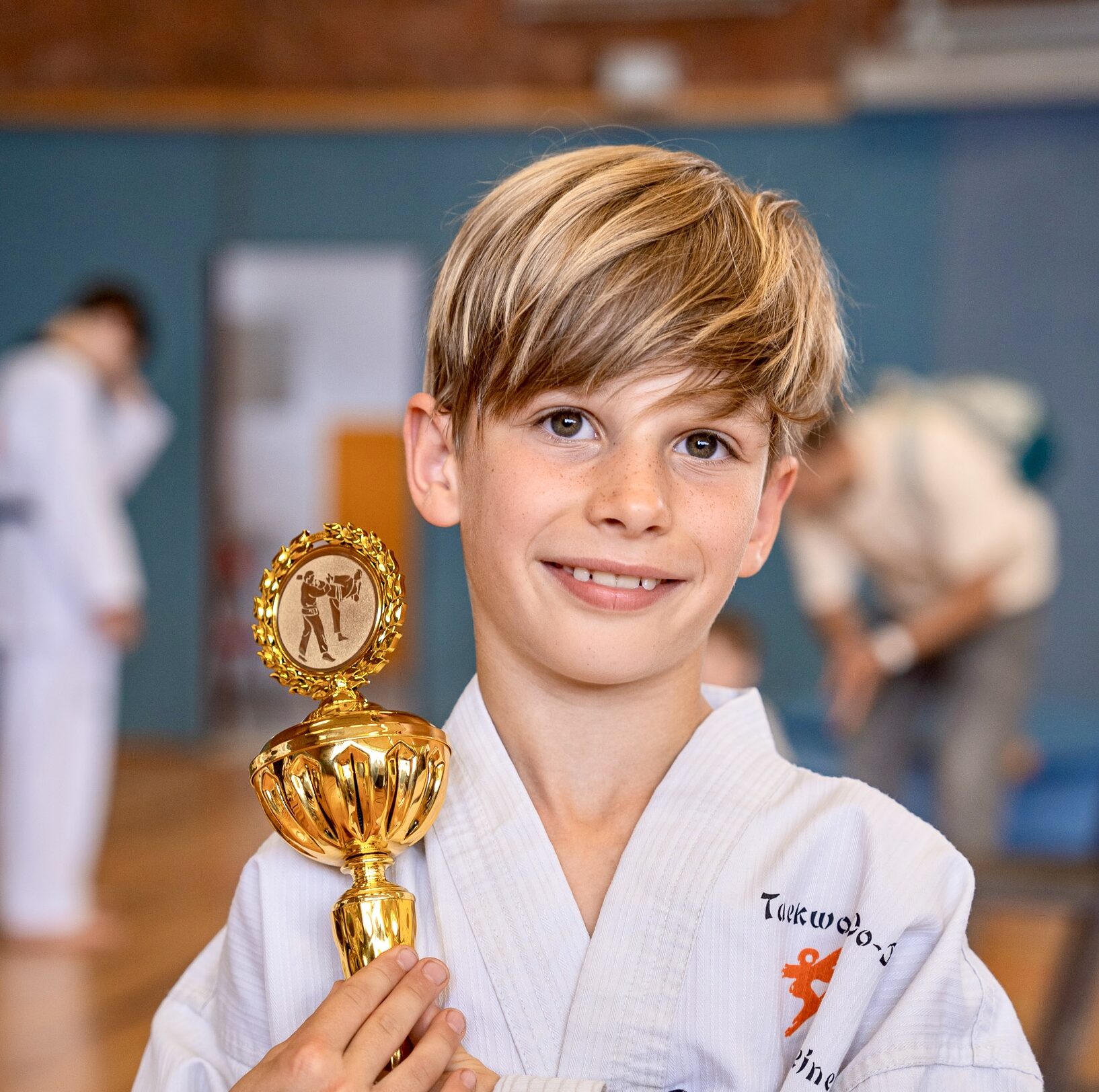 Ein Kind freut sich ueber seinen Pokal bei einem Taekwondo-Turnier